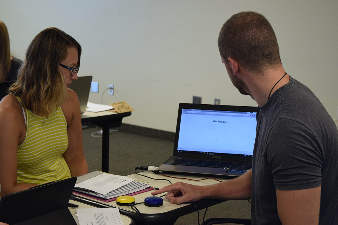 Two occupational therapy students using Scanning Wizard. One is pressing a switch with his hand to select items from the computer screen